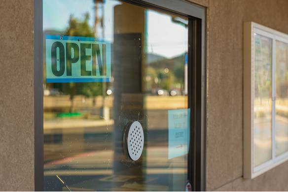A glass door with an "OPEN" sign is shown, reflecting the street and trees outside. A white intercom or speaker is attached to the glass.