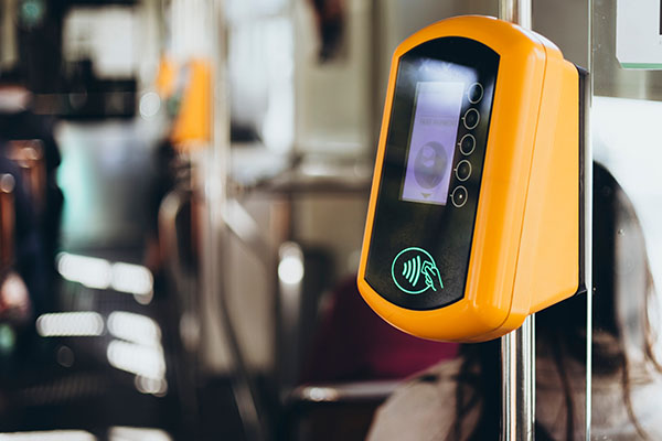 A close-up of a yellow contactless card reader on public transport, displaying a lit NFC payment symbol.