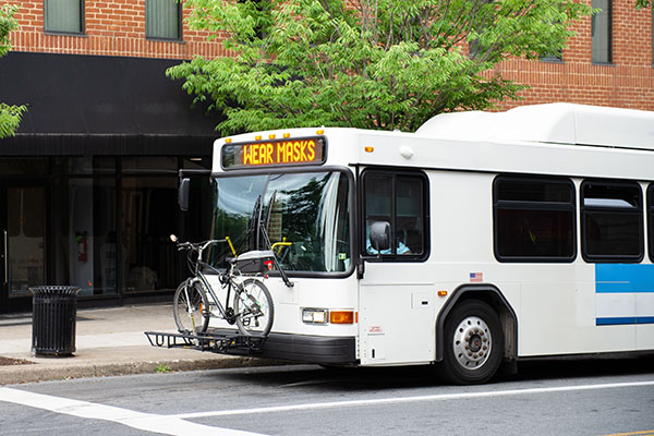 A city bus with a digital sign reading "WEAR MASKS" is parked at a curb, carrying a bicycle on its front-mounted bike rack.